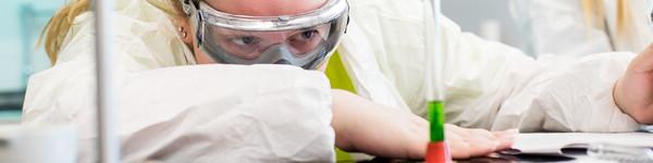 Female student in a lab leans down to observe and record results in a test tube.